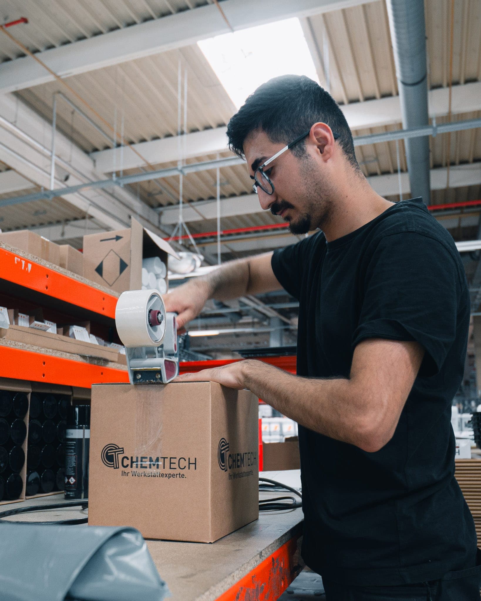 Ein Mann verklebt im Lager einen Versandkarton mit ChemTech-Logo